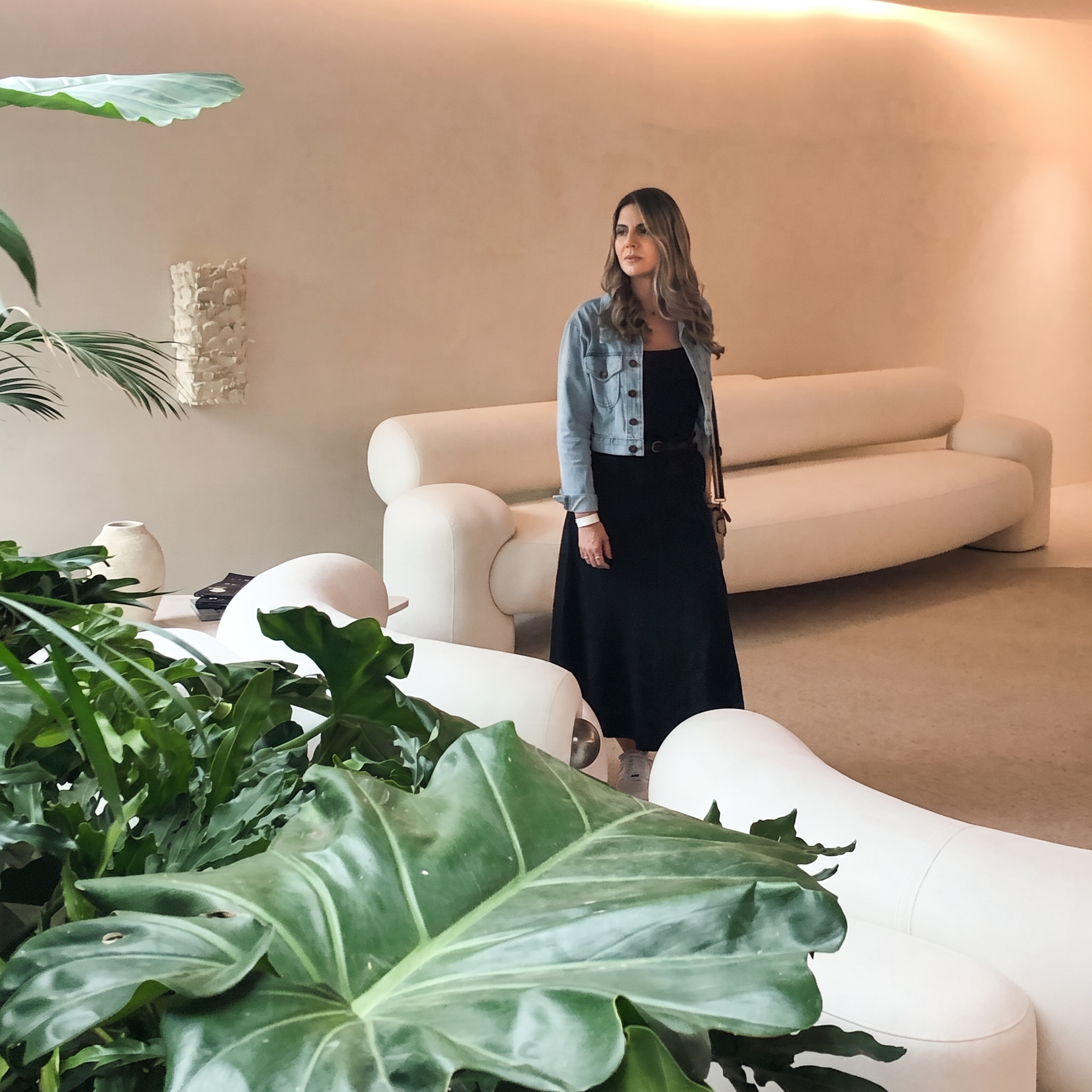 Joyce Brigagão, arquiteta, em ambiente de tons terrosos com sofá curvo e plantas